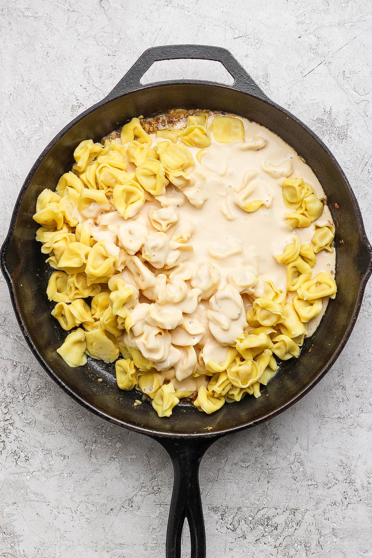 Cooked tortellini and alfredo sauce in a cast iron skillet.