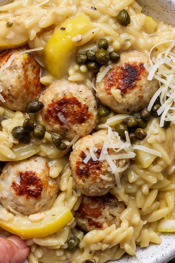 A bowl of chicken piccata meatballs in orzo with capers and parmesan cheese.