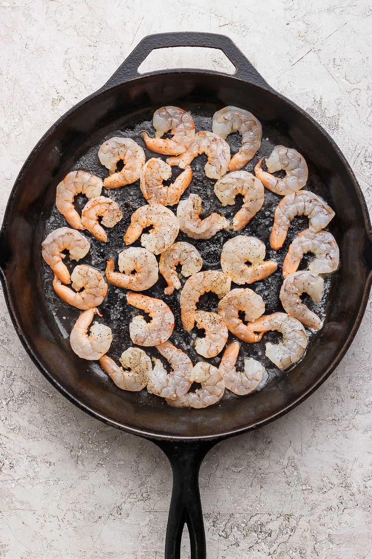 Uncooked shrimp in a cast iron skillet with salt and pepper on top.