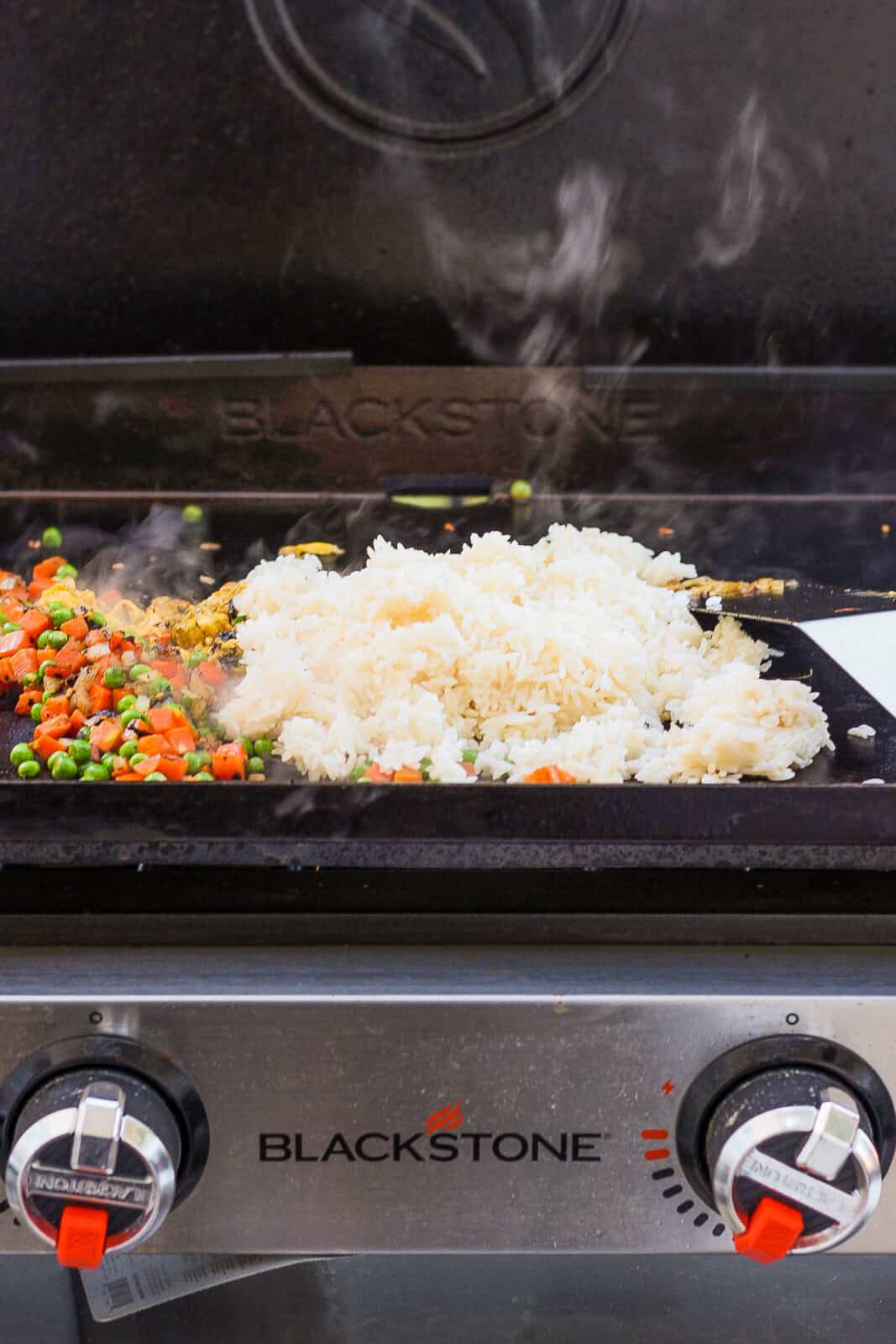 Cold rice added to the Blackstone griddle next to cooked peas and carrots.