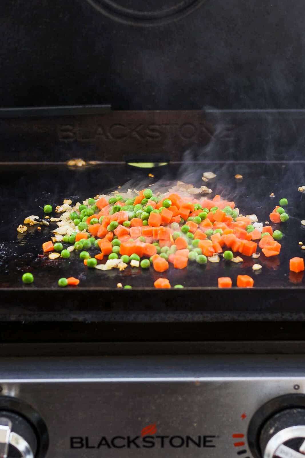 Onions, garlic, peas, and carrots cooking on a Blackstone griddle.