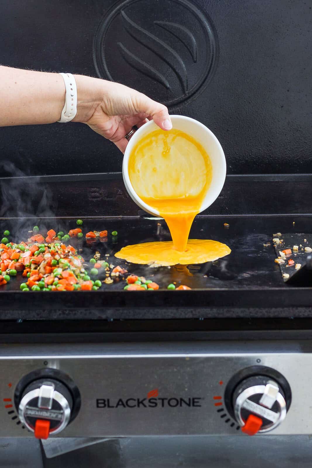Whisked eggs being poured from a white bowl on to the Blackstone griddle.