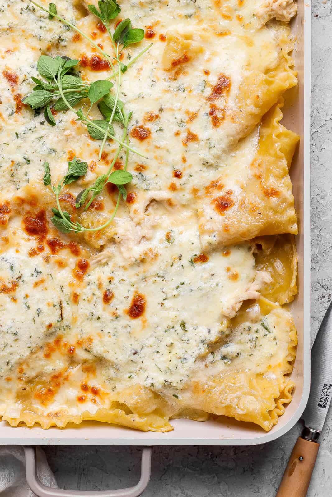 The corner of a fully baked chicken alfredo sheet pan lasagna with a knife next to it.