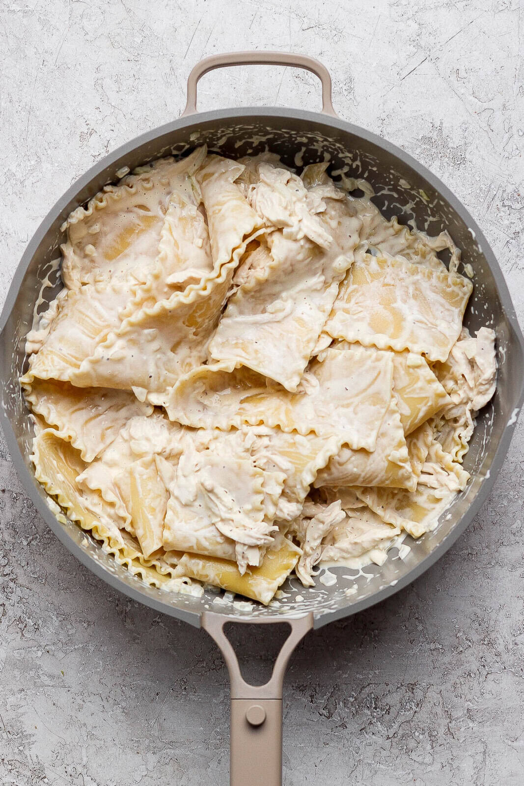 Cooked lasagna noodles added to the chicken alfredo mixture in a skillet.