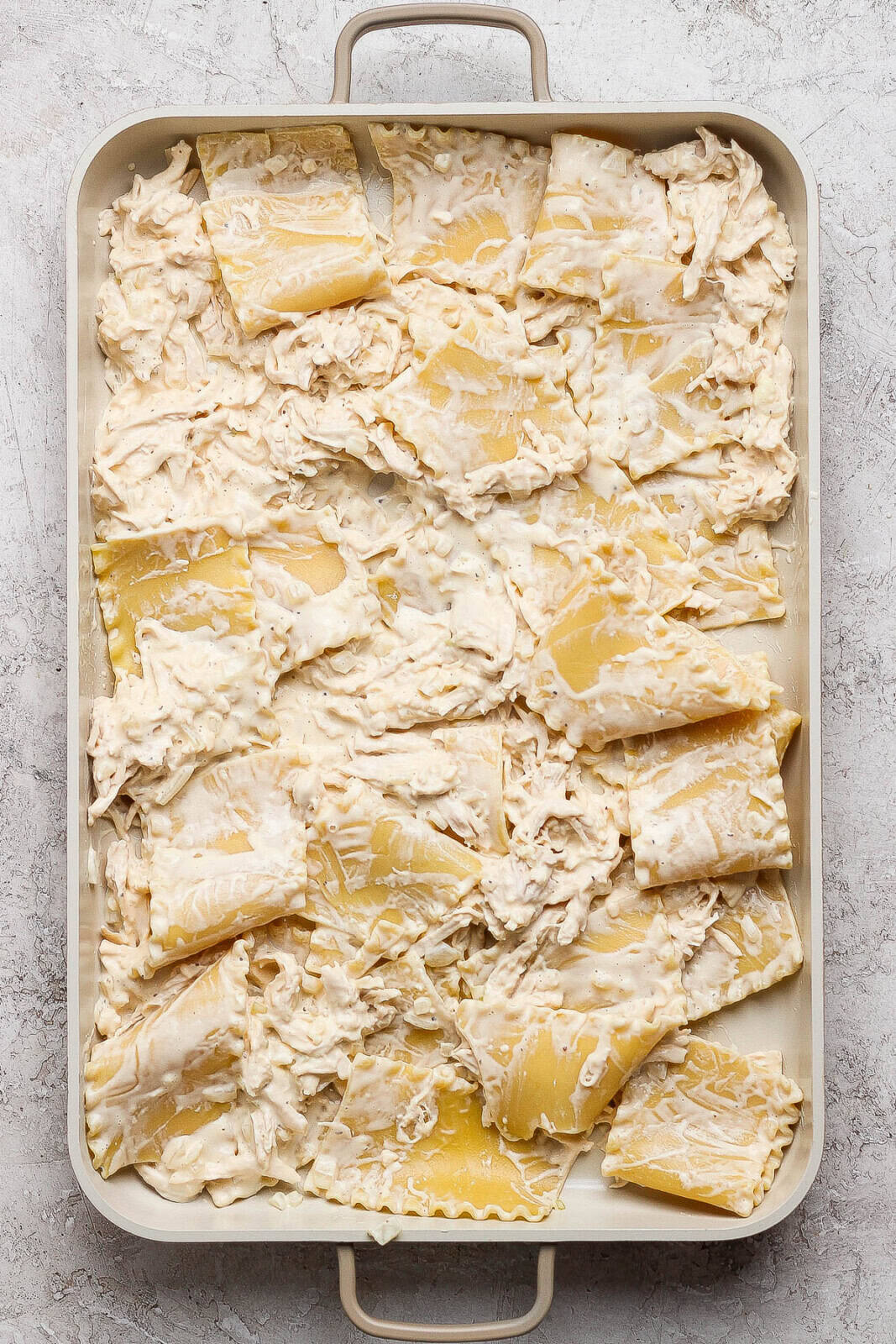 Chicken alfredo lasagna mixture spread in a deep sheet pan.