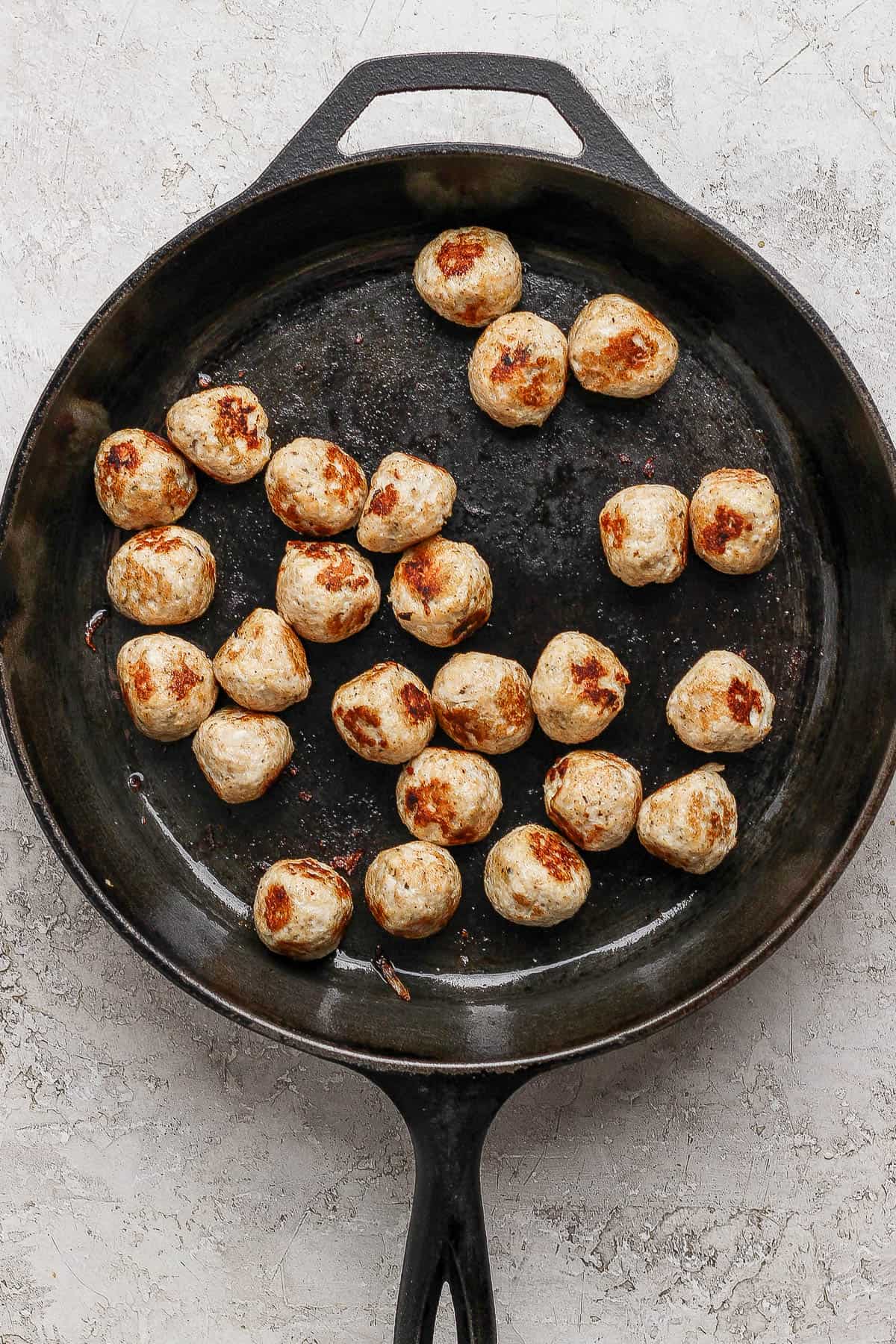 Chicken meatballs cooking in a cast iron skillet.