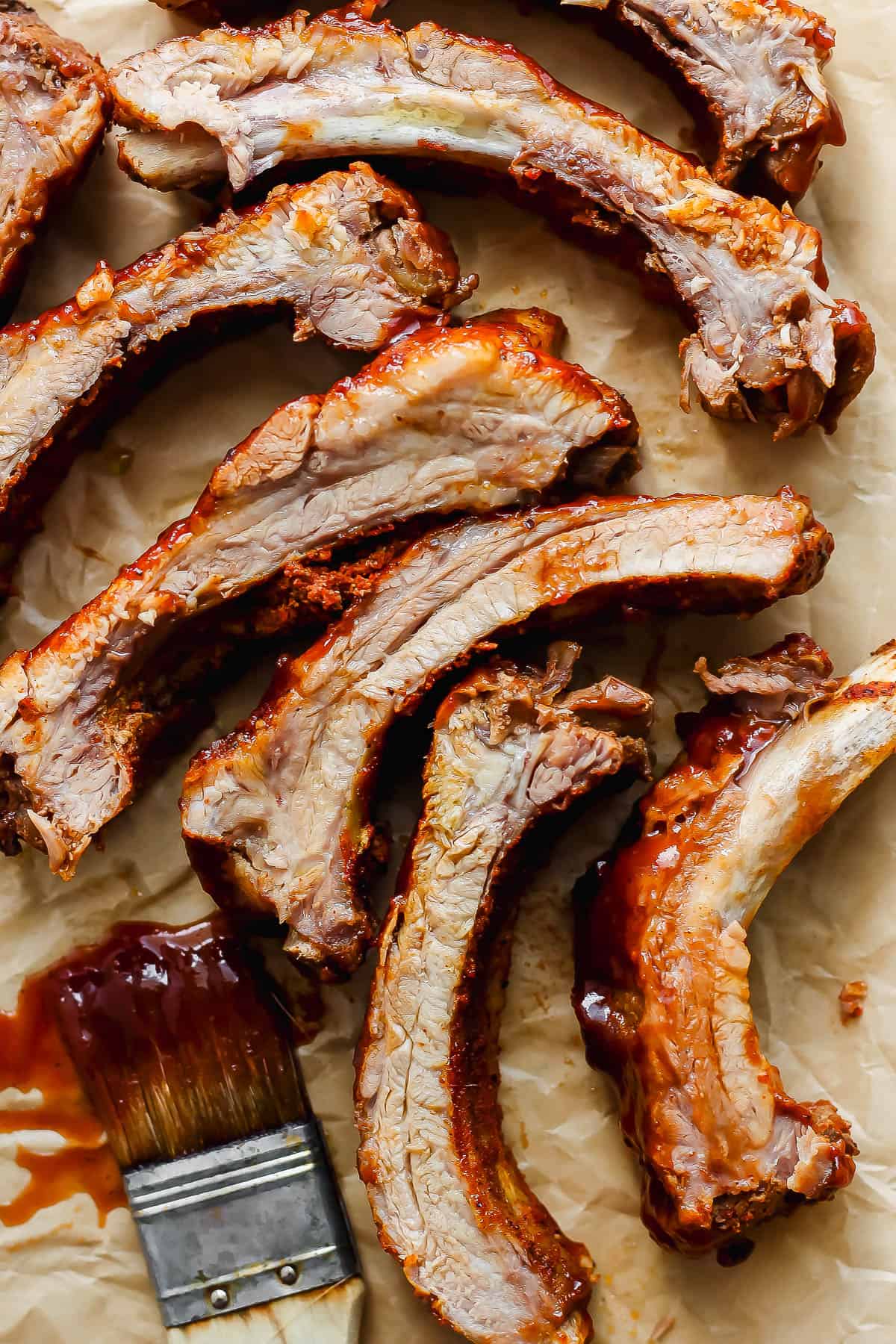 Several separated Instant Pot ribs on a piece of parchment paper with a basting brush covered in bbq sauce.