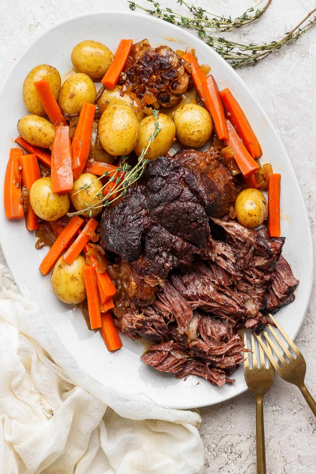 Shredded pot roast on a platter with potatoes and carrots.