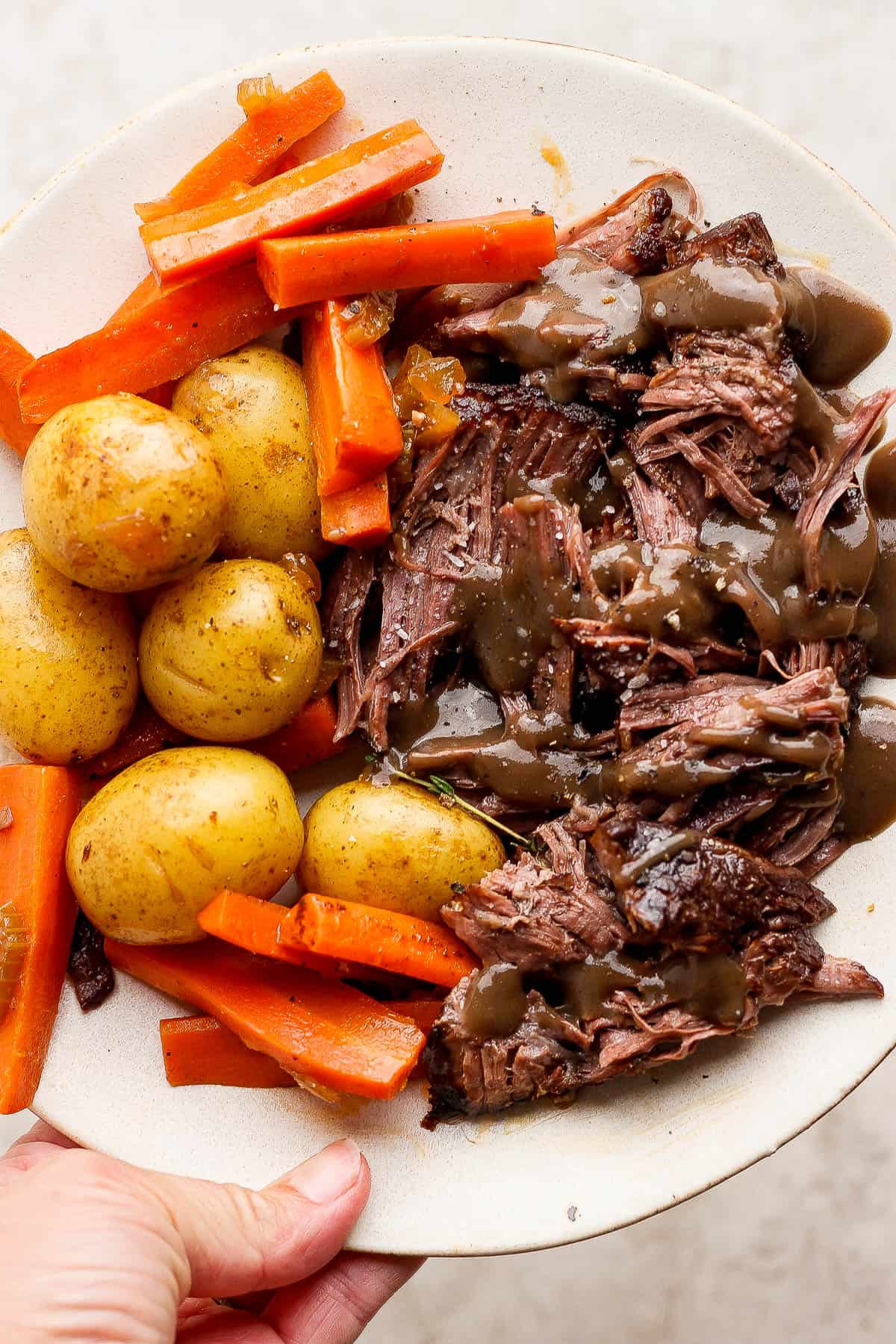 Shredded pot roast on a plate with potatoes, carrots, and gravy on top.