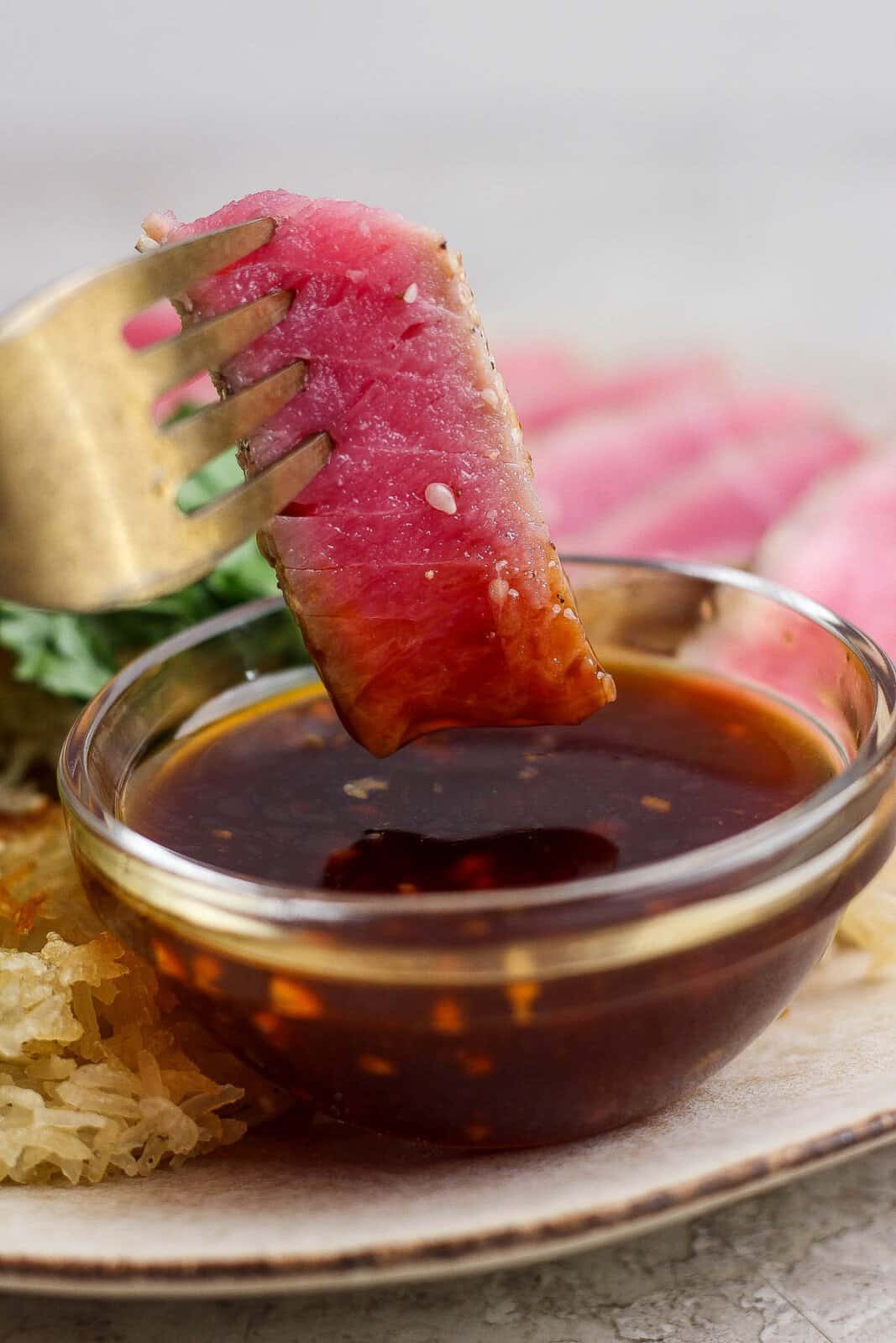 A slice of seared ahi tuna being dipped in a sauce with a fork.