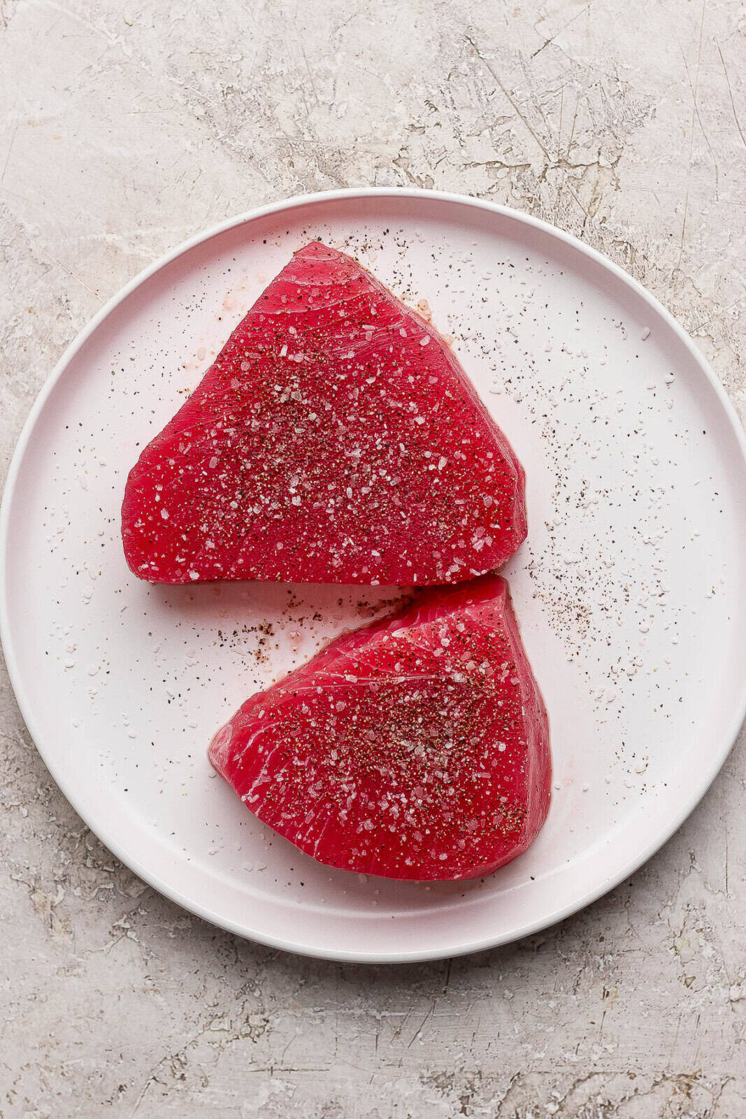 Tuna steaks on a white plate seasoned with salt and pepper.