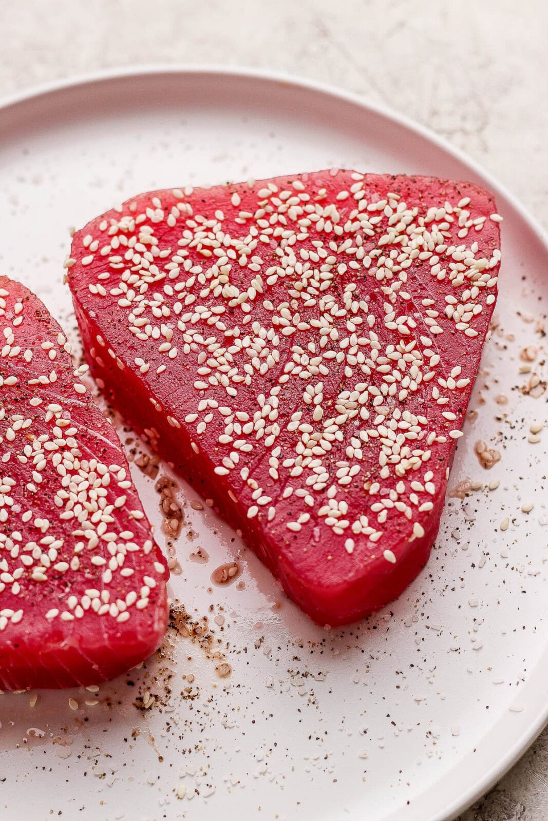 Seasoned tuna steaks on a white plate with sesame seeds pressed into them.
