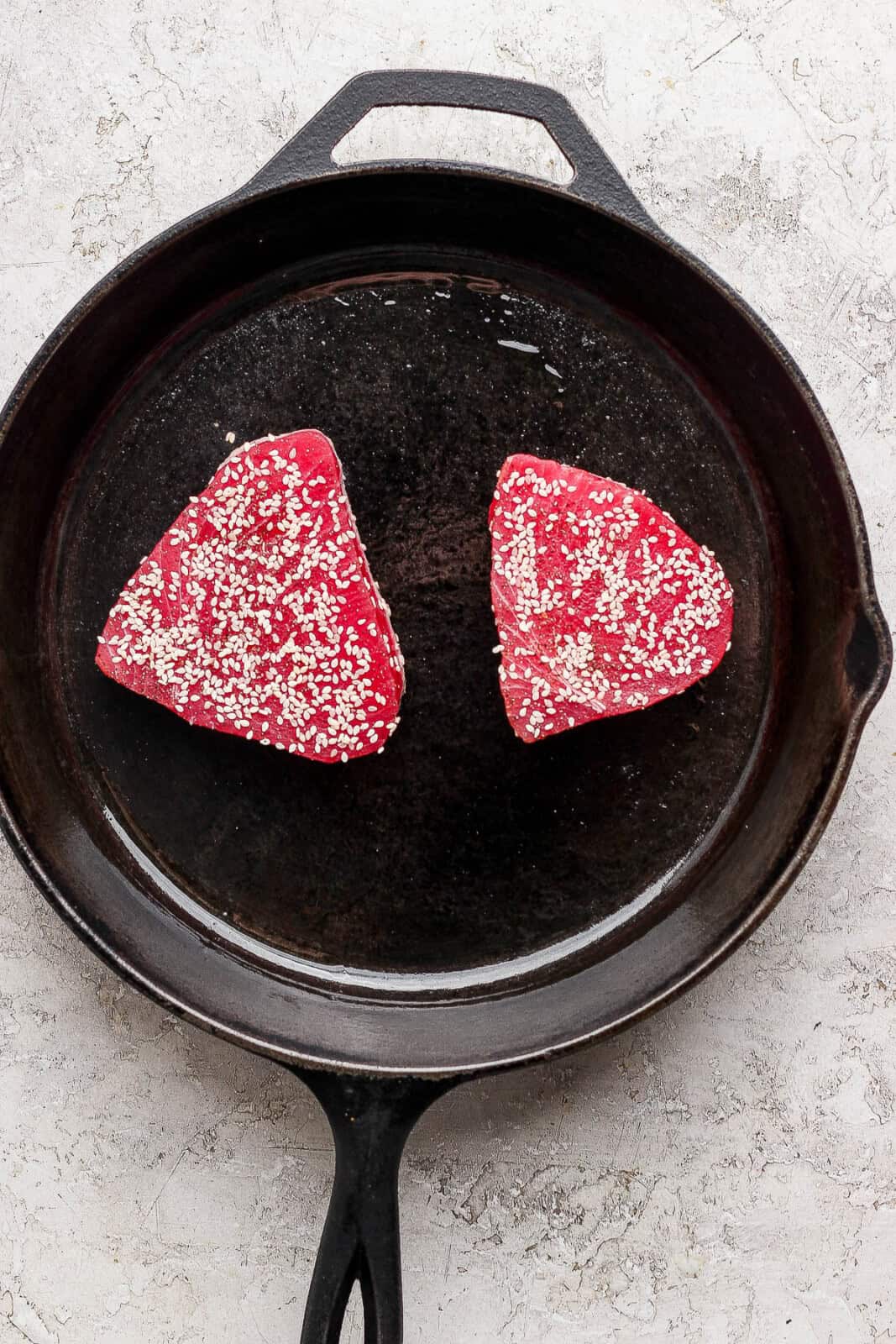 Two seasoned tuna steaks searing in a large cast iron skillet.
