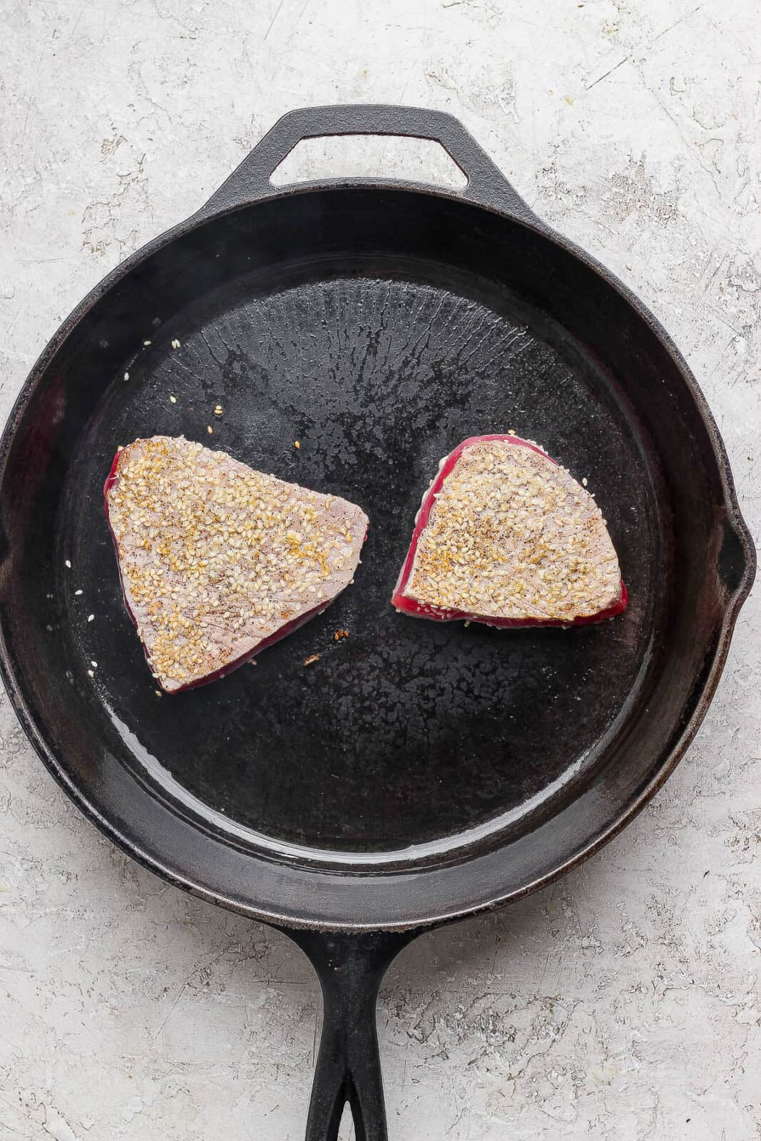 Two seasoned tuna steaks searing in a cast iron skillet after being flipped once.