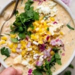 A bowl of mexican street corn white chicken chili with fresh cilantro, red onion and crumbled feta cheese on top.