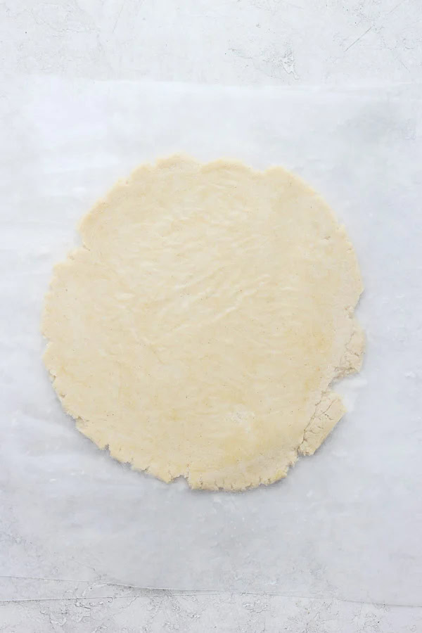 A gluten free pie crust rolled out in between two pieces of wax paper.