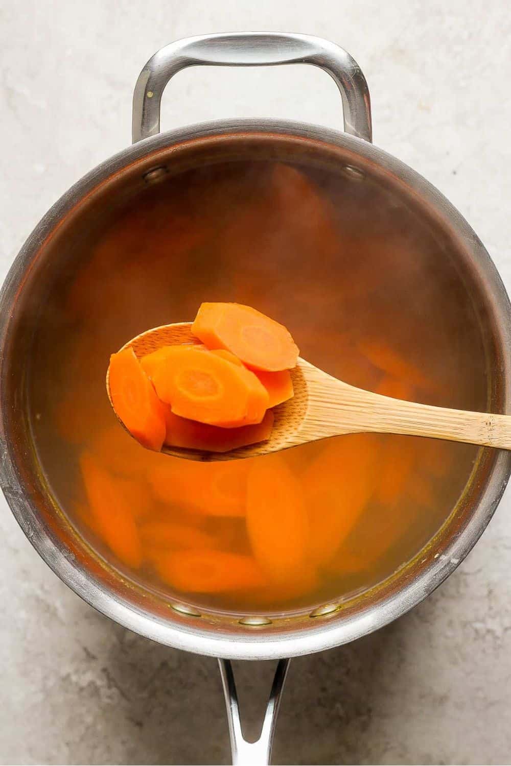 A wooden spoon scooping a few cooked sliced carrots.