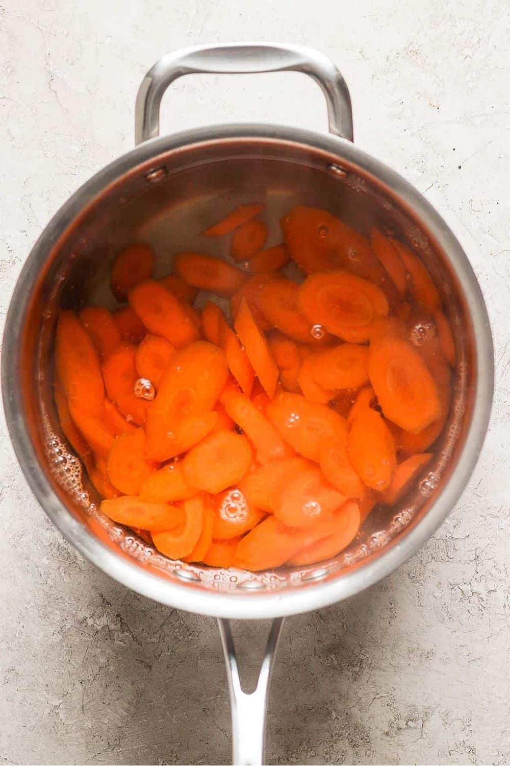 Sliced carrots boiling in a sauce pan with water.