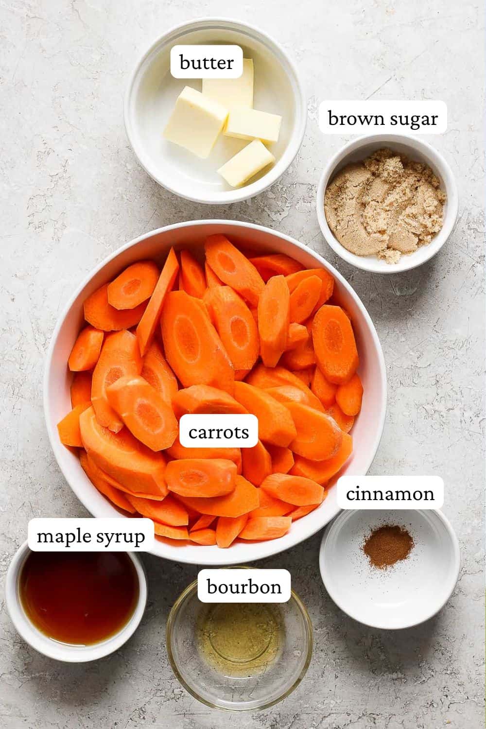 Individual bowls of butter, brown sugar, sliced carrots, ground cinnamon, maple syrup, and burbon.