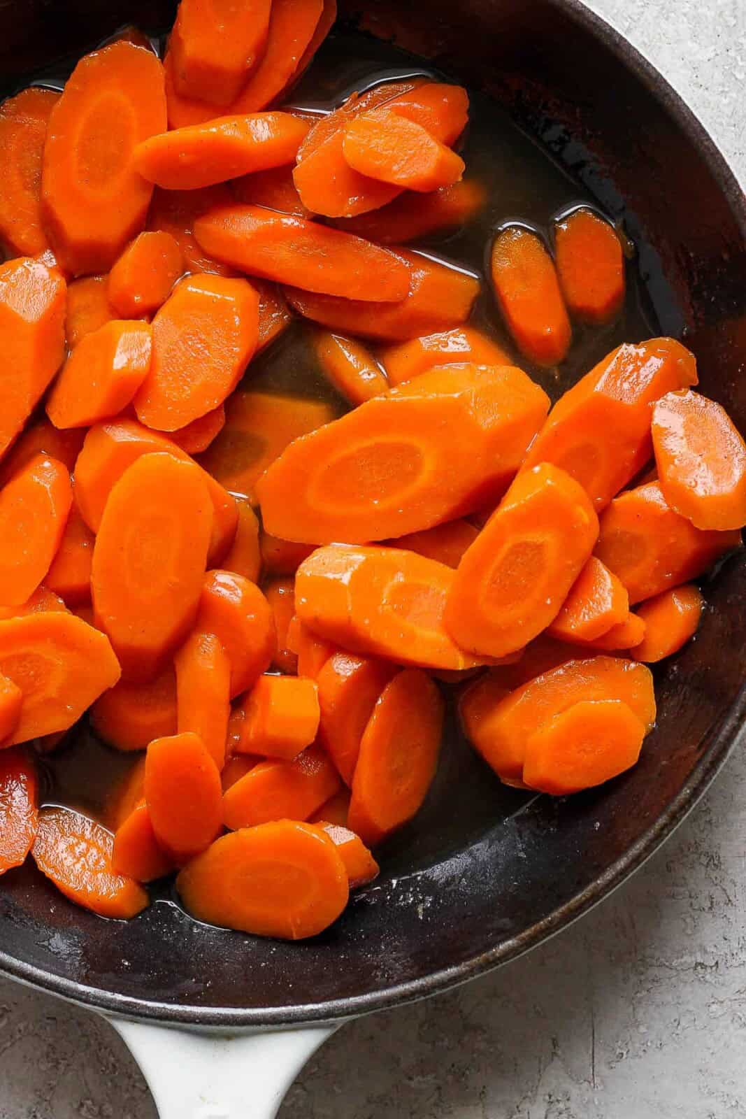 Cooked sliced carrots tossed in brown sugar glaze in cast iron skillet.