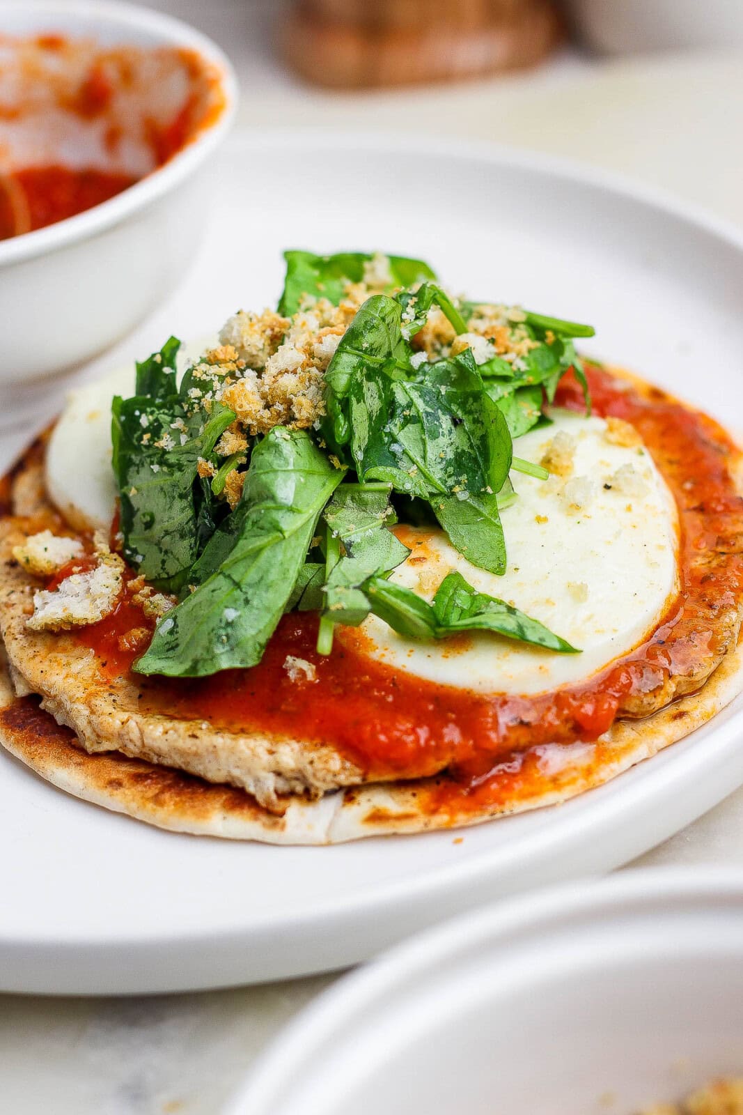 A chicken parm smash taco sitting on a plate with fresh arugula, basil, and crushed croutons on top.