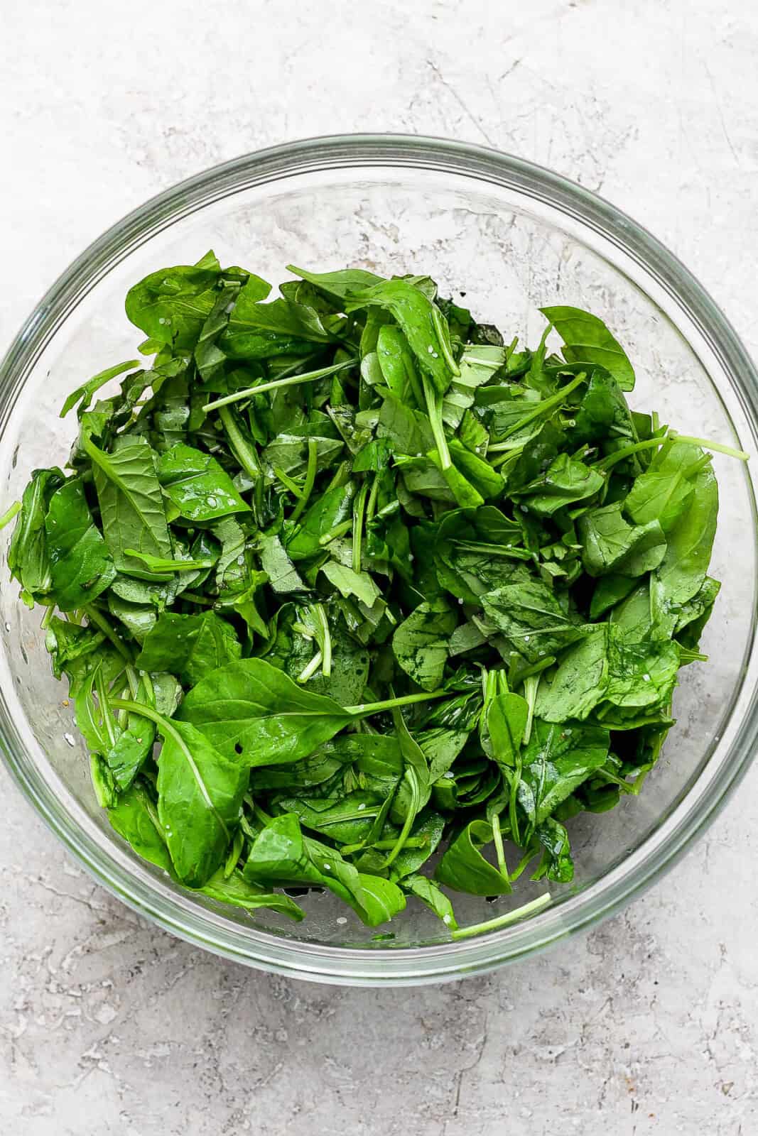 Freshly chopped arugula and basil leaves in a large glass bowl with a drizzle of olive oil, salt, and pepper.