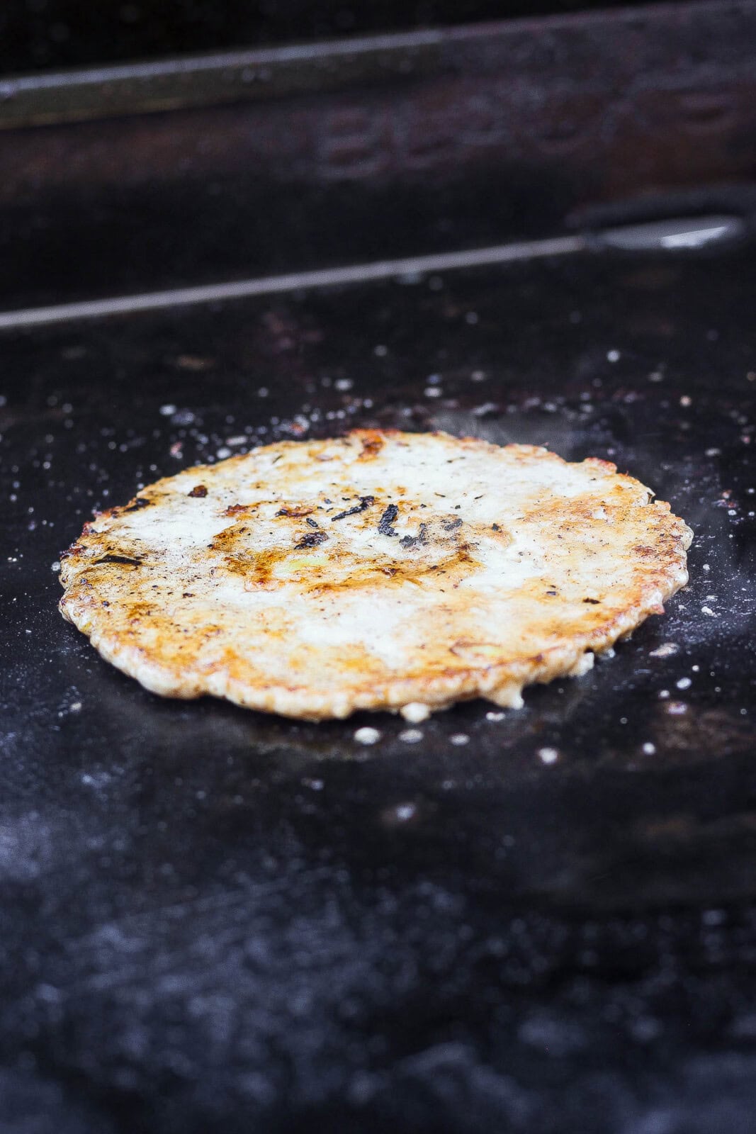 A smashed chicken burger on a hot griddle cooktop.