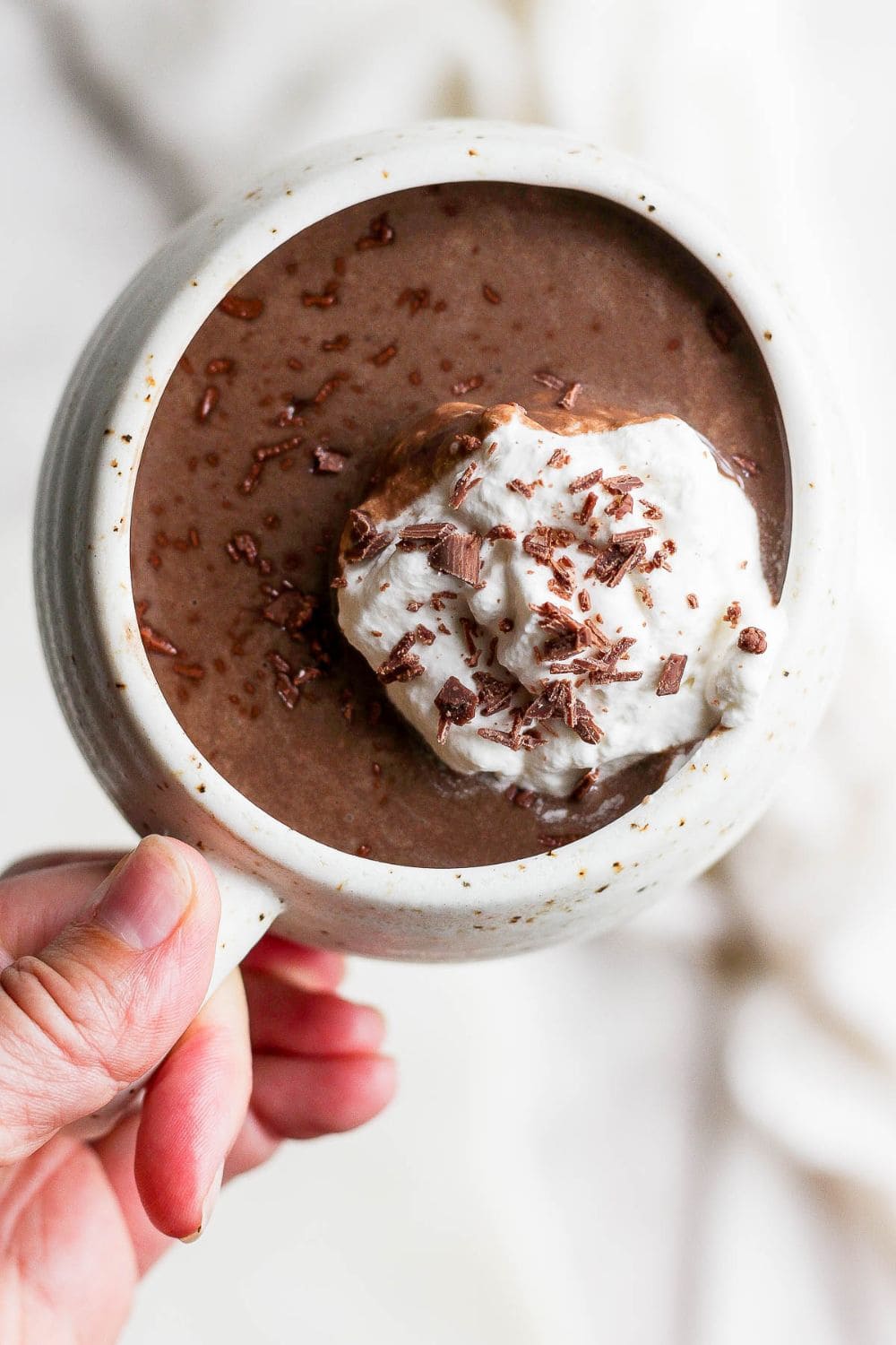 A mug with crock pot hot chocolate topped with whipped cream and chocolate shavings.