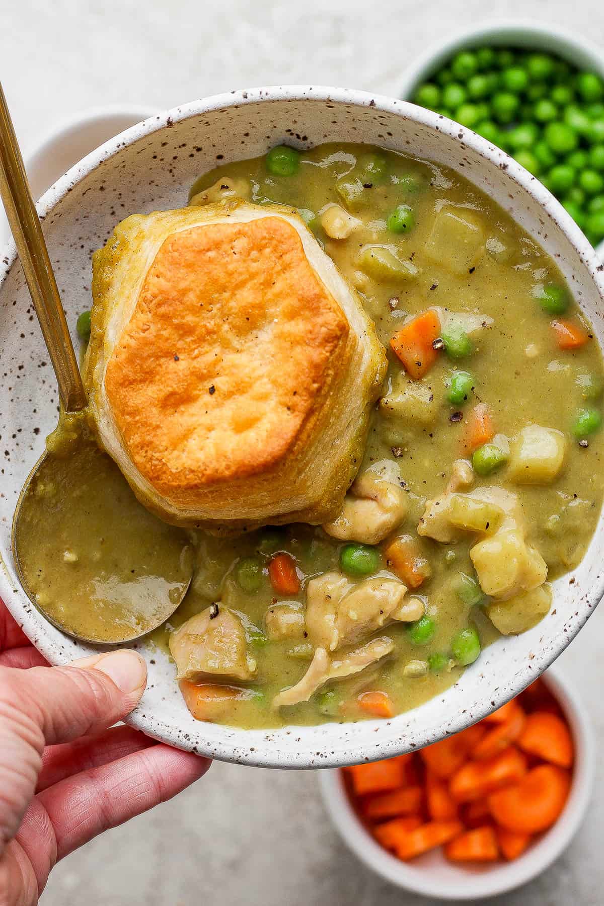 A bowl of chicken curry pot pie topped with a biscuit and a spoon sticking out the side of the bowl.