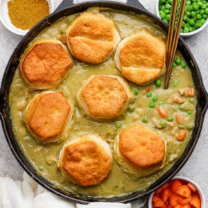 A chicken curry pot pie in a skillet with biscuits and two spoons sticking out, fully cooked.