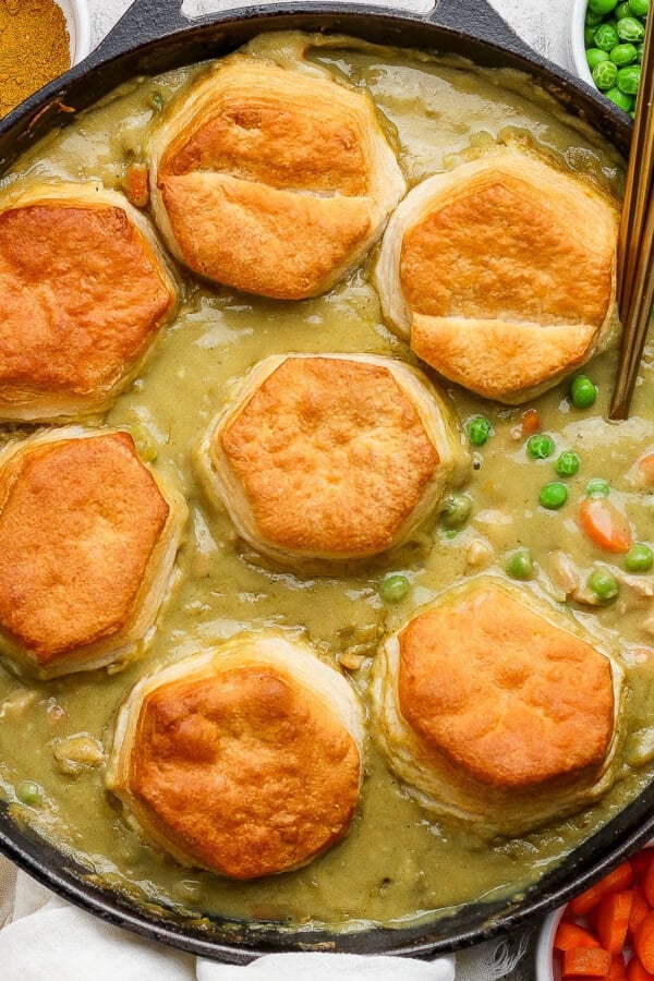 A chicken curry pot pie in a skillet with biscuits and two spoons sticking out, fully cooked.