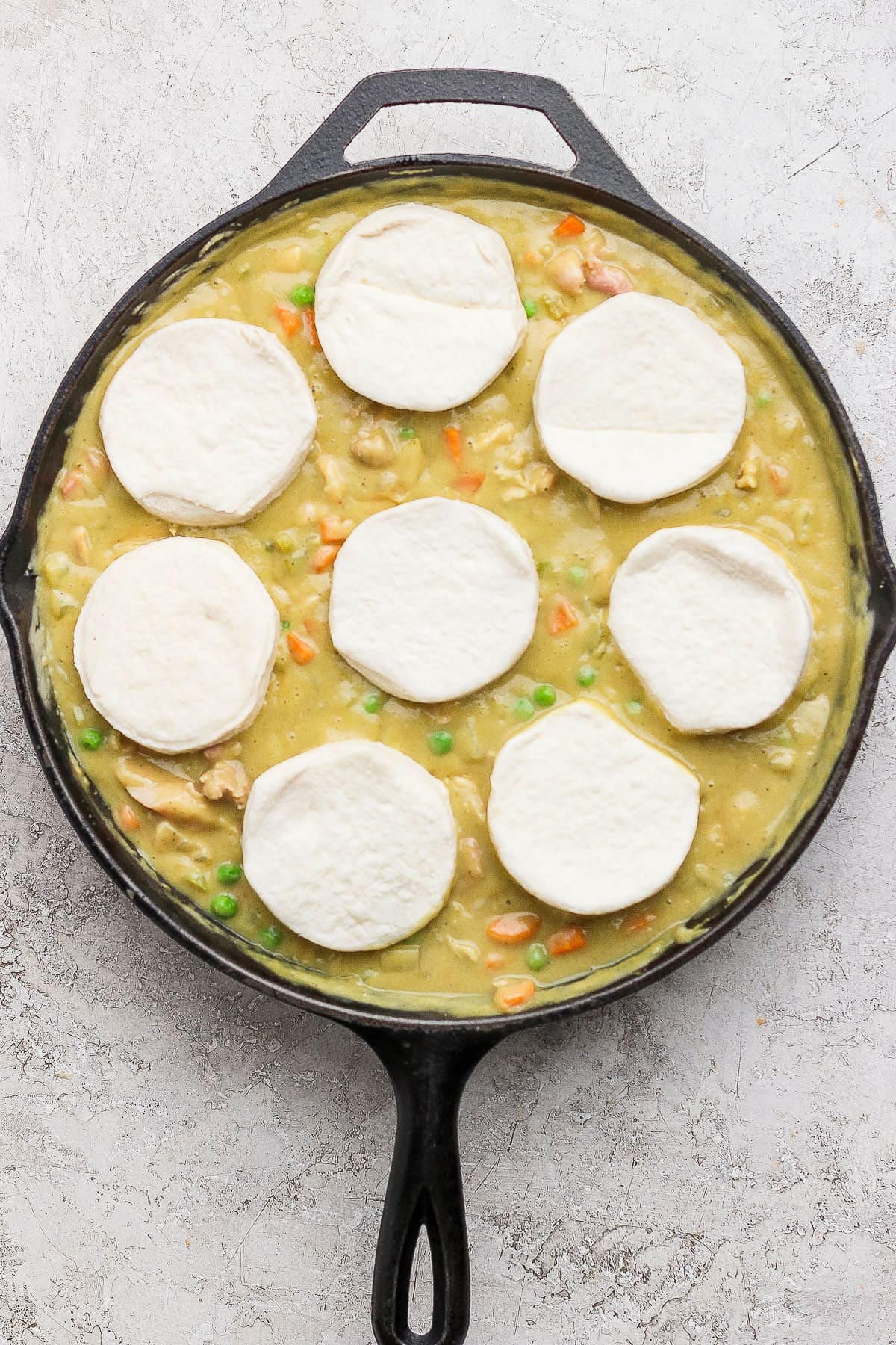 Eight raw biscuits on top of the curry chicken pot pie filling in a skillet.