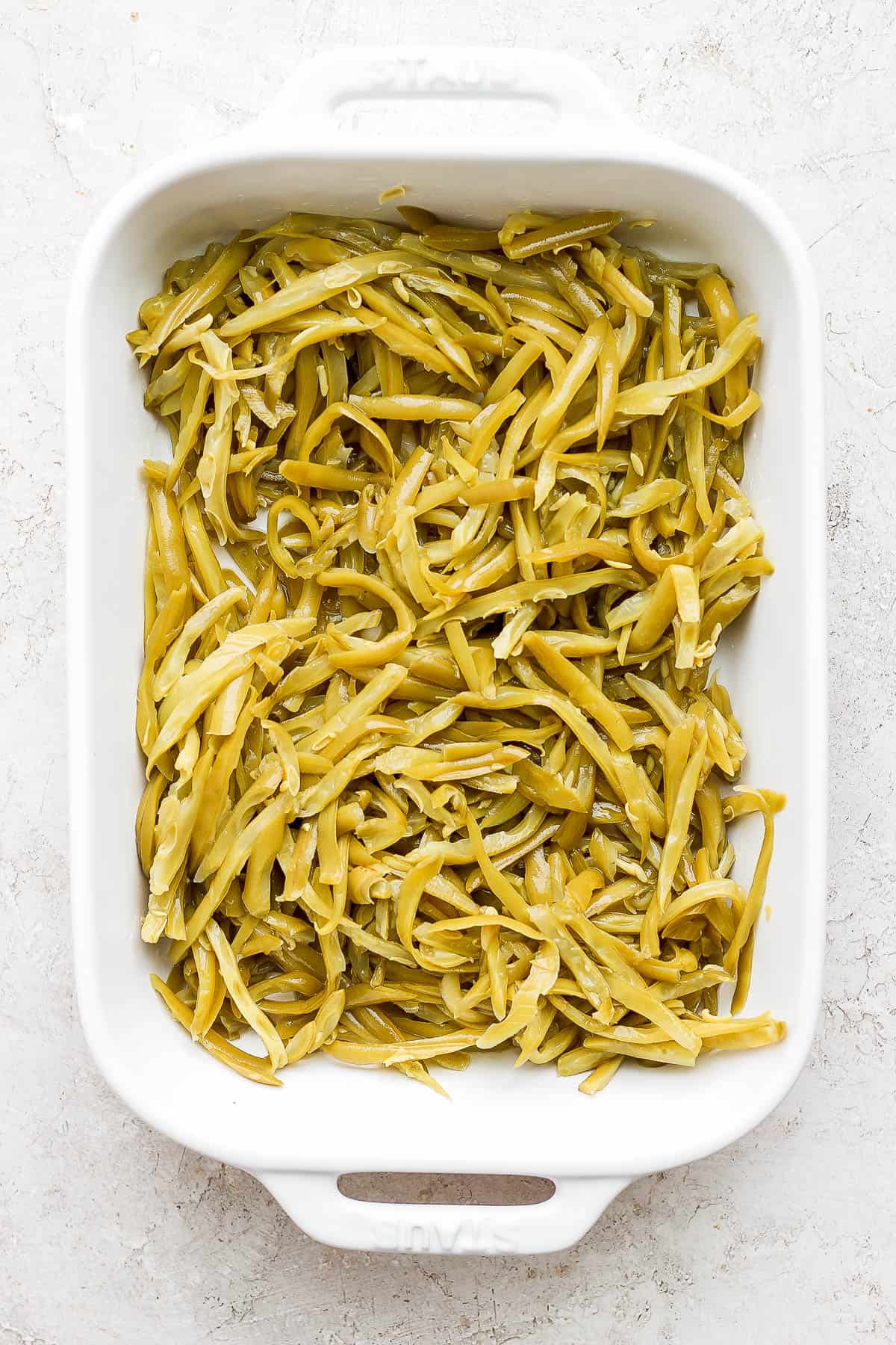 French-cut canned green beans spread in a white baking dish.