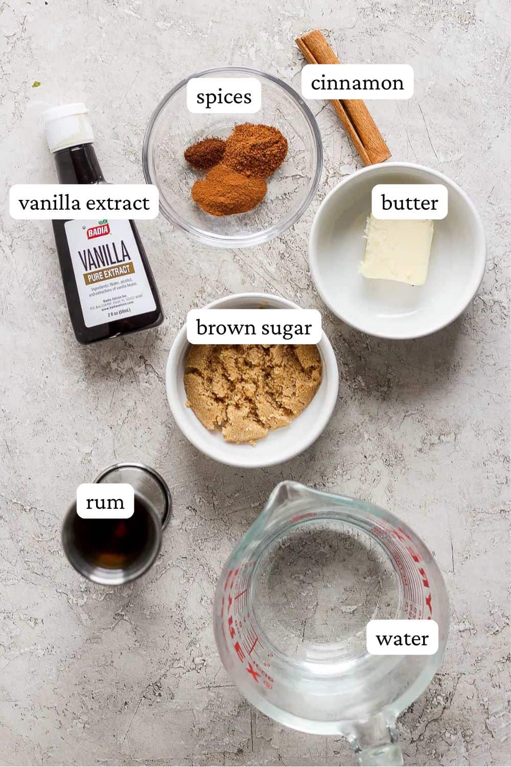 Ingredient shot showing spices, a cinnamon stick, butter, brown sugar, vanilla extract, rum, and water.