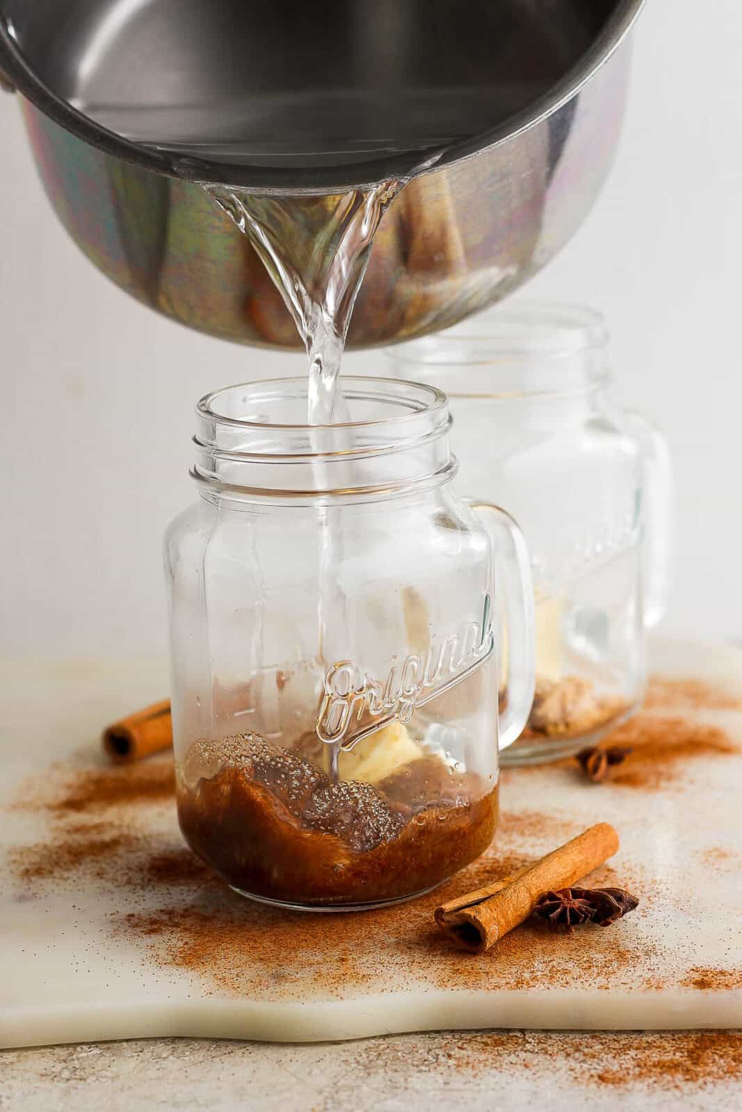Butter, brown sugar, cinnamon, cloves, nutmeg, vanilla extract, and rum added to a glass mug.