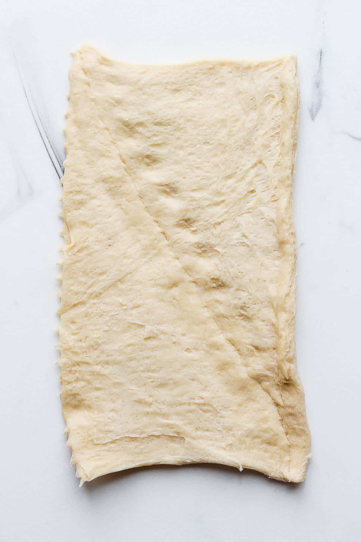 A section of crescent roll dough with the seam pinched together on a marble board.