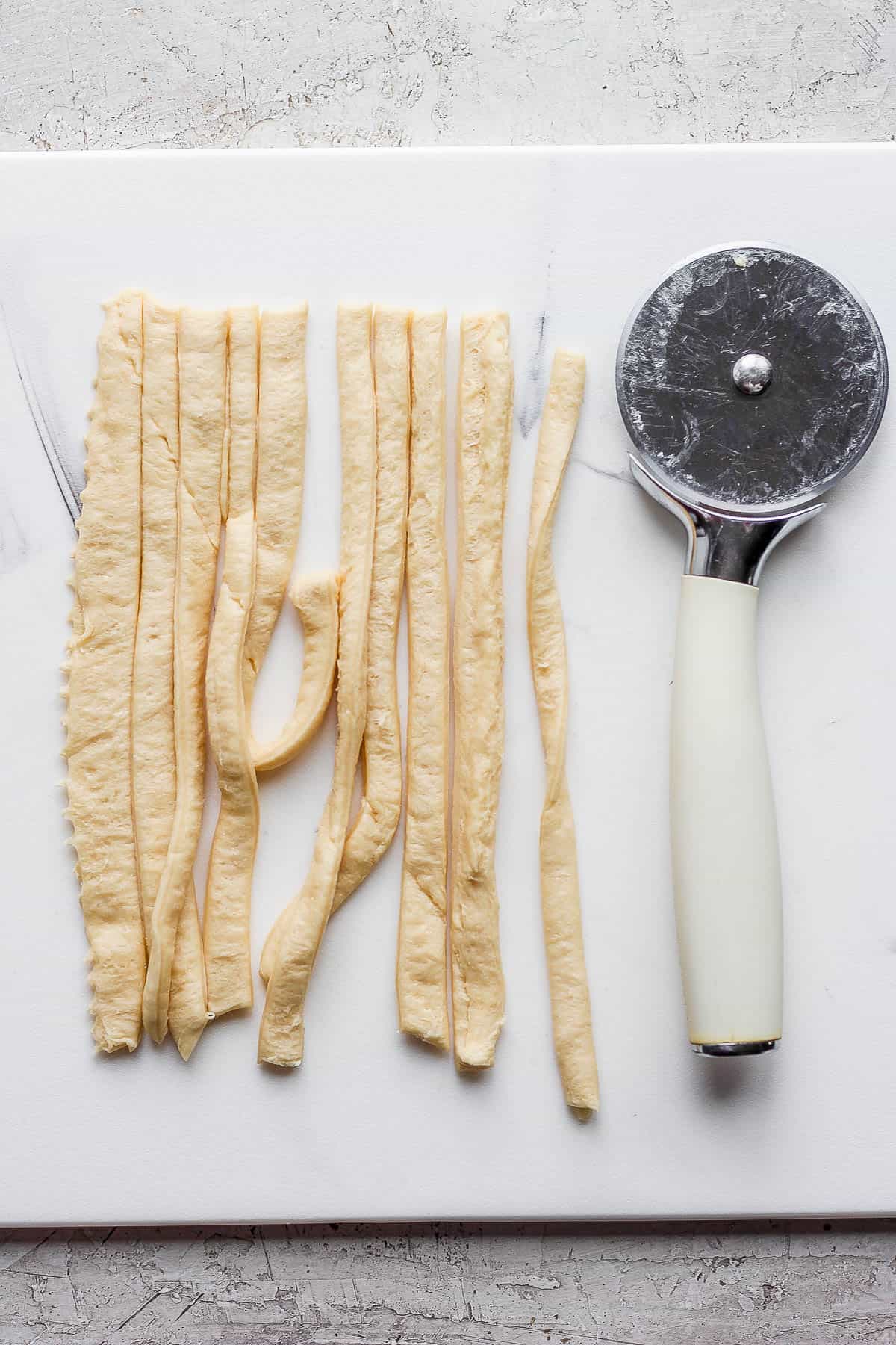 A section of crescent roll dough cut into strips next to a pizza cutter.