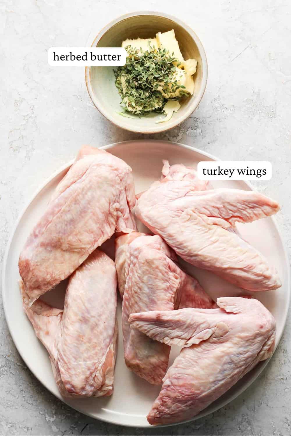 Raw turkey wings on a white plate next to a small bowl of herb butter, unmixed, plus text labels for each one.