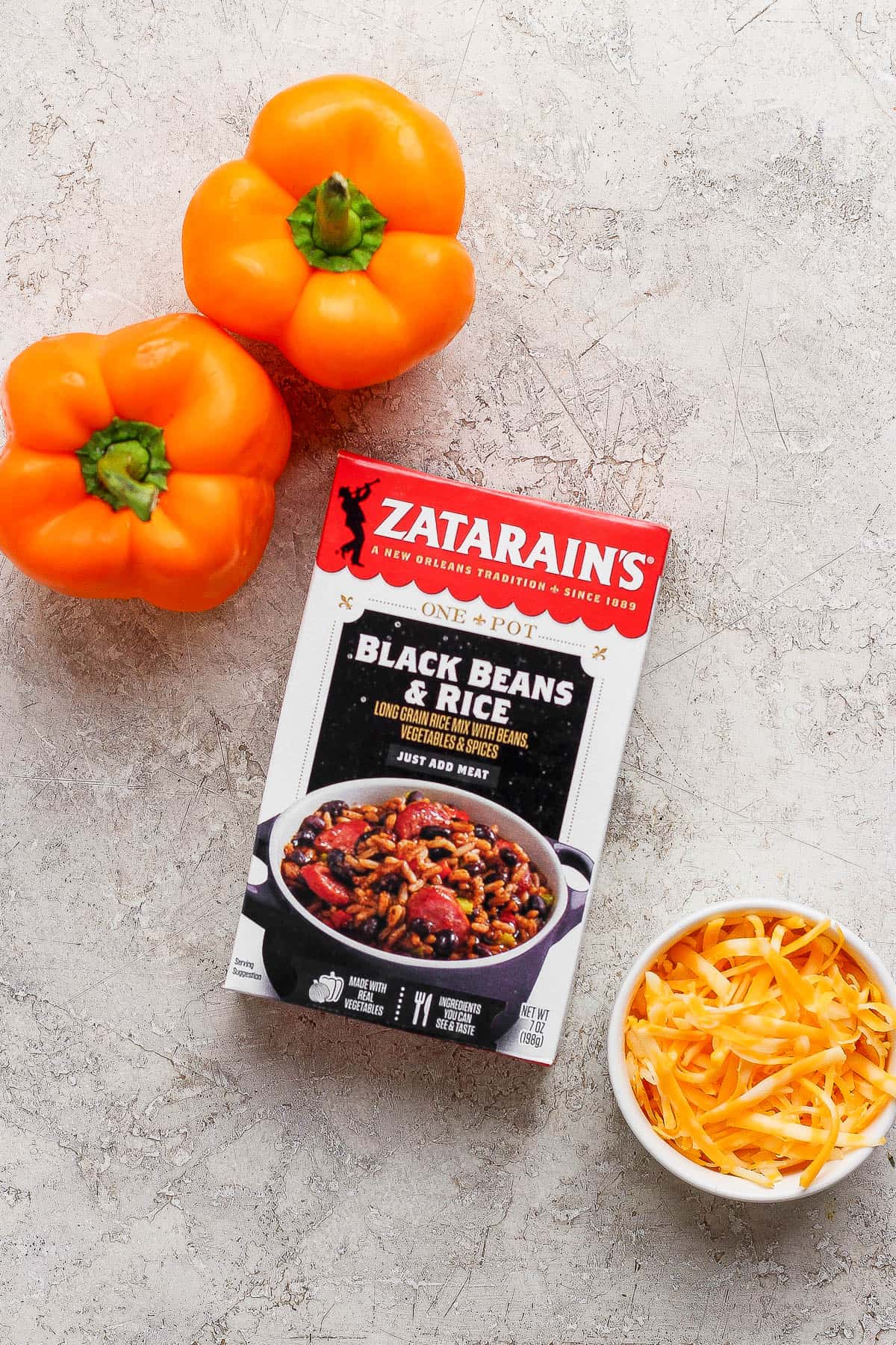 A box of Zatarain's black beans and rice with two orange bell peppers and a small dish of shredded cheese.