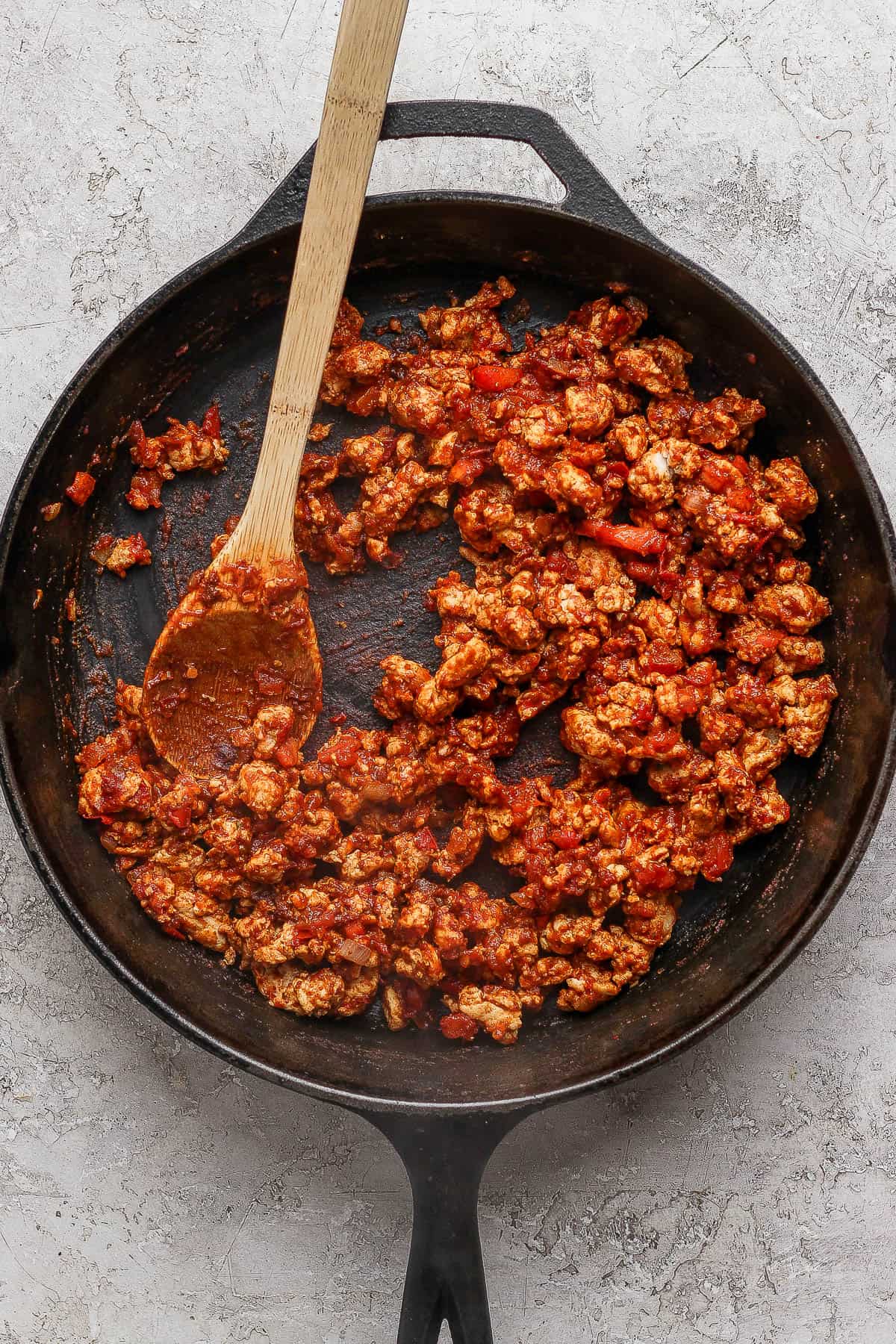 A cast iron skillet with the fully cooked filling mixture for jack-o-lantern stuffed peppers with a wooden spoon sticking out the side.