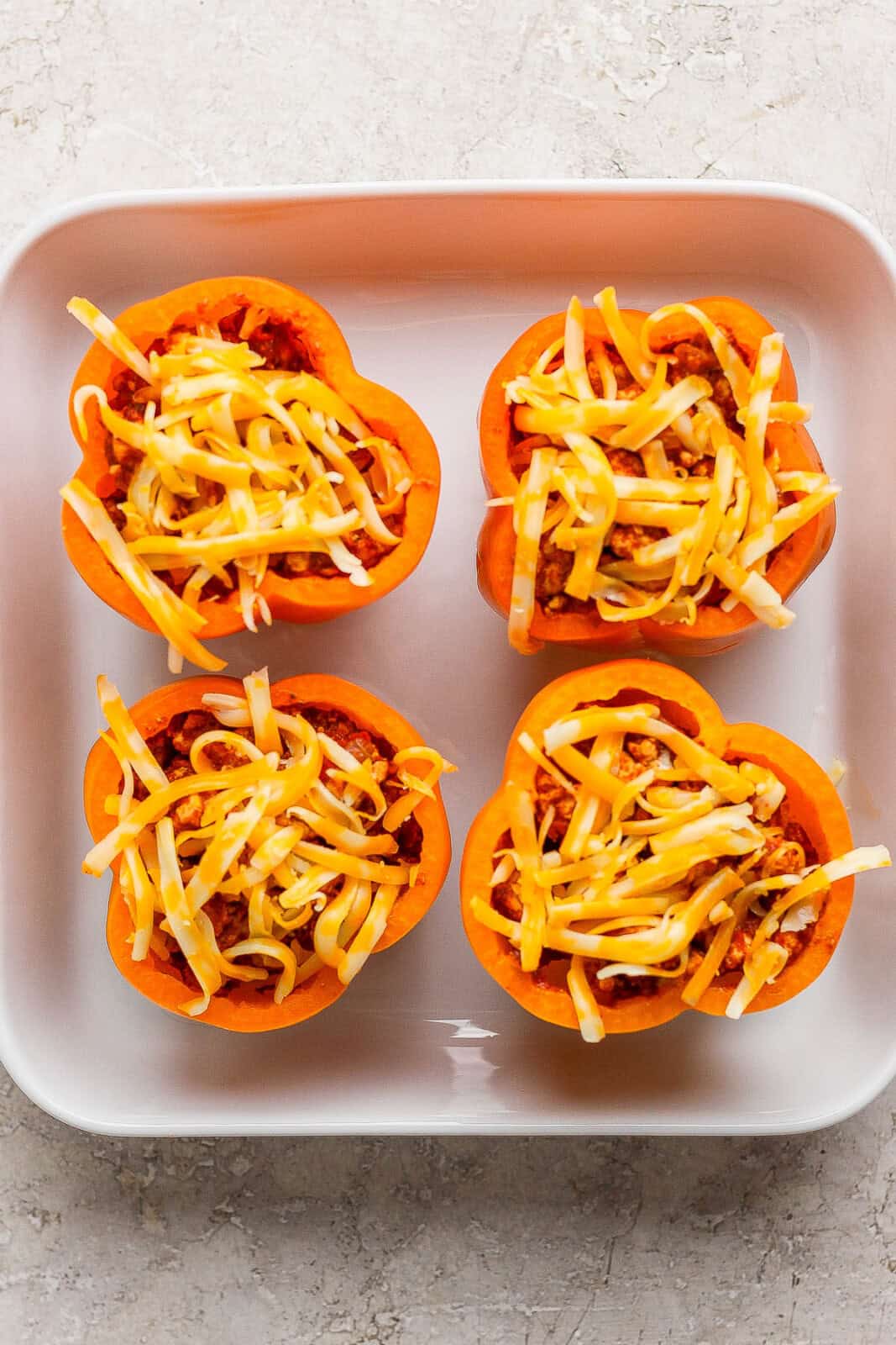 Four jack-o-lantern stuffed peppers in a white baking dish with cheese sprinkled on top.