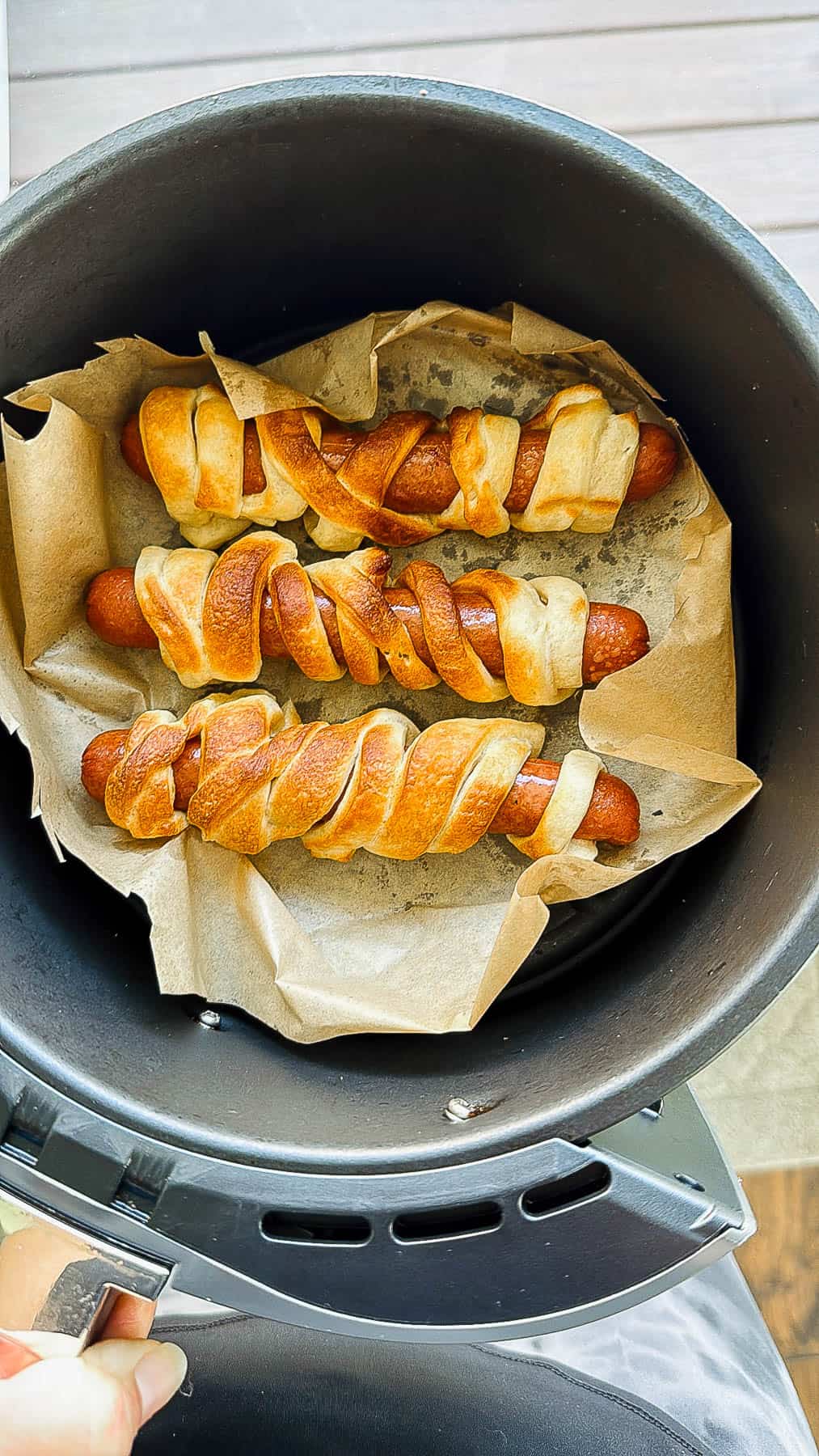 Three mummy hot dogs in a parchment-lined air fryer basket after being cooked.