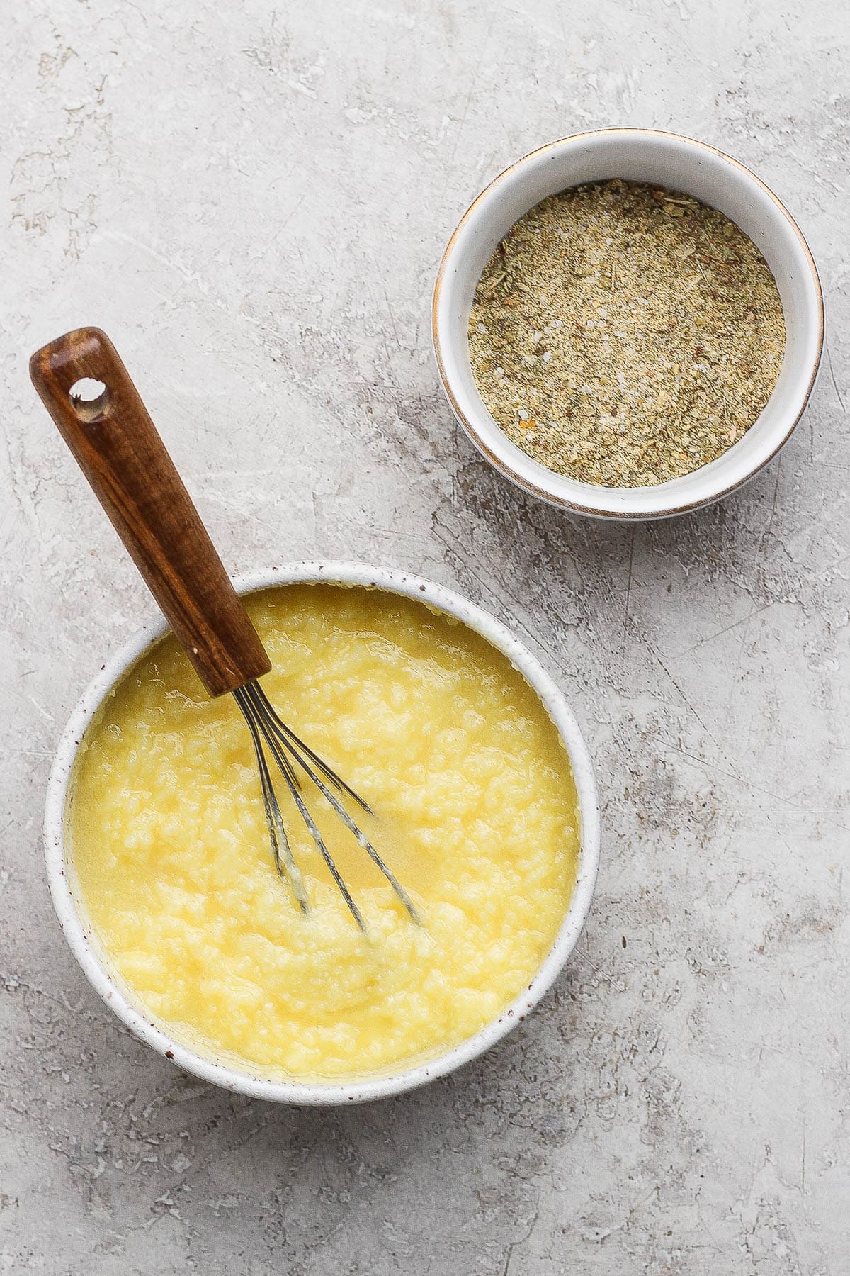 A small bowl of turkey dry rub next to a bowl of turkey basting liquid with a whisk sticking out of it.