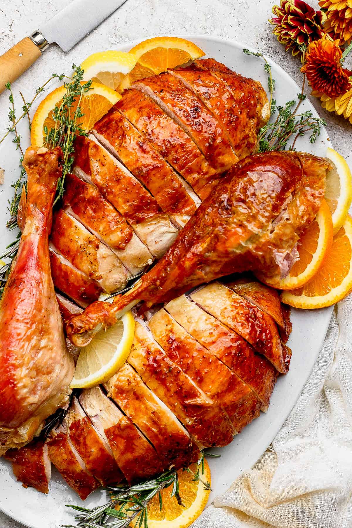 Carved orange turkey breasts and turkey legs on a large white platter with orange slices, lemon slices, and fresh thyme.