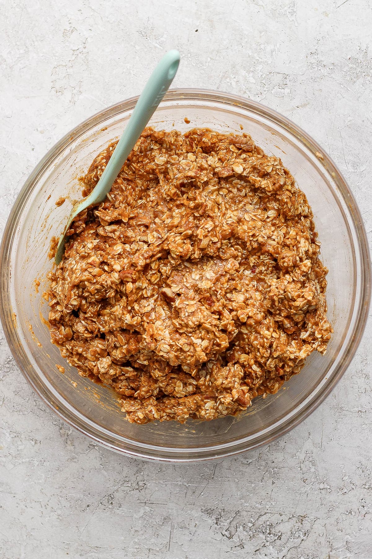 Pumpkin baked oatmeal ingredients mixed together in a glass bowl with a rubber spatula.