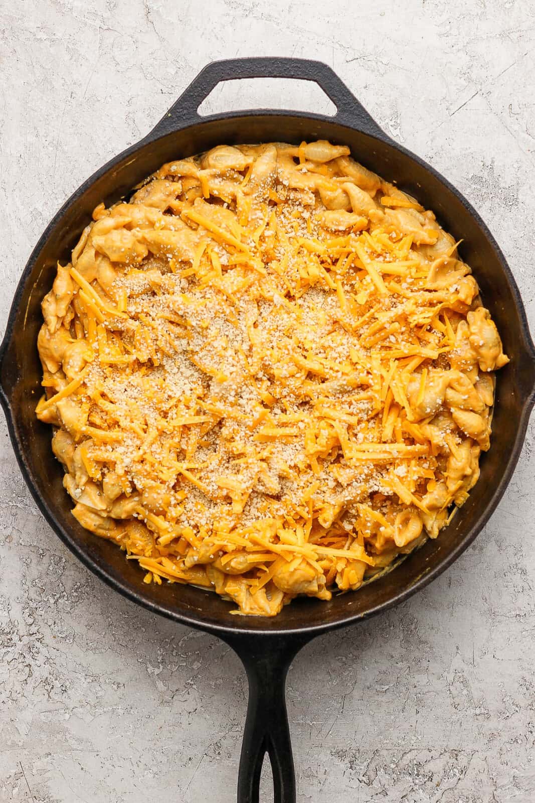 The noodles fully mixed with the cheese sauce and topped with remaining shredded cheese and panko bread crumbs.