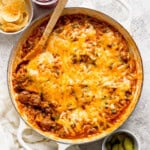 Fully cooked sloppy joe orzo in a braiser pan with a wooden spoon in it.