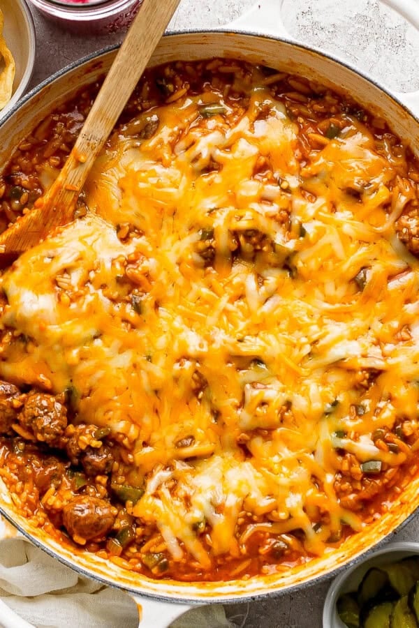 Fully cooked sloppy joe orzo in a braiser pan with a wooden spoon in it.