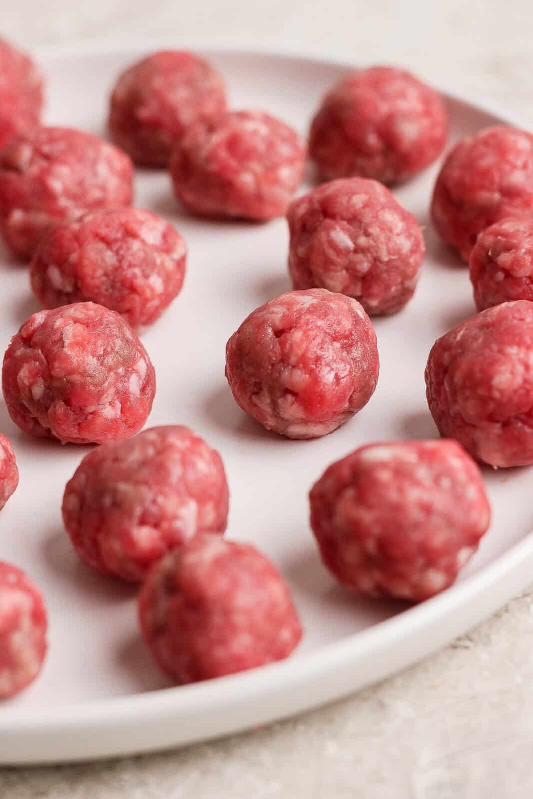 Rolled mini meatballs on a white plate before cooking.
