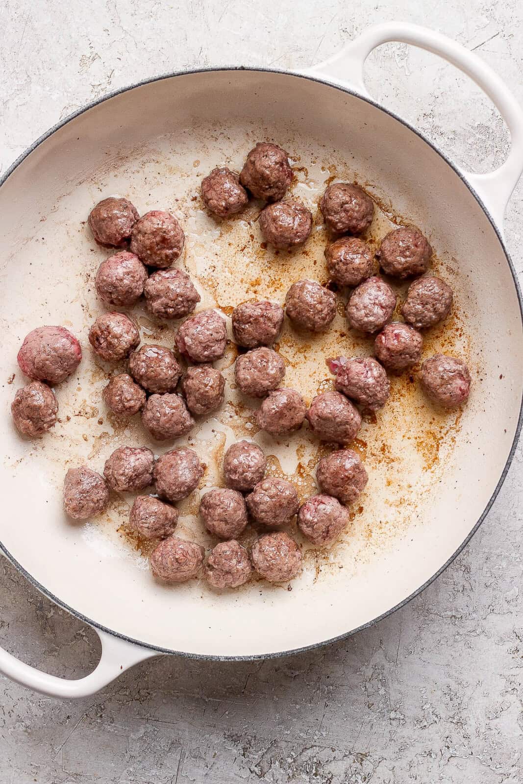 A white braising pan with meatballs searing in it.